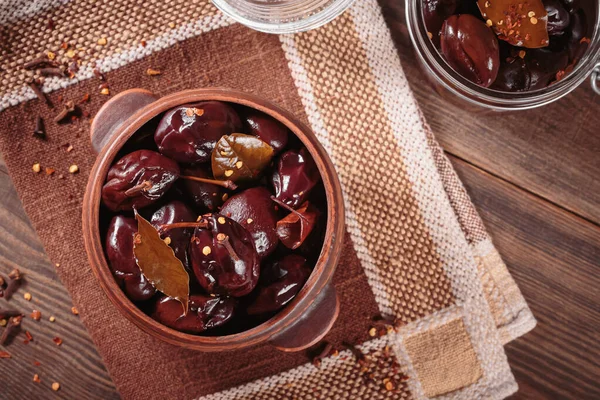 Bowl of pickled plums with spices on rustic wooden background. Clean eating, vegetarian food concept