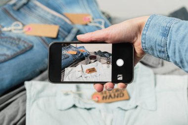 Kadın elinin kot kıyafetlerin fotoğrafını çekerek akıllı telefondan ikinci el moda uygulamasını yüklediği görüntüler. İnternette giysileri sat, al ve değiş tokuş et.