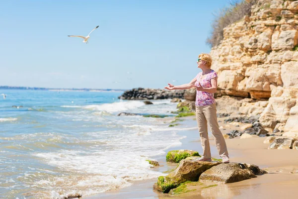 Stock image Senior woman in sunglasses stands on the beach and looks at the sea. Old woman enjoying life near the sea