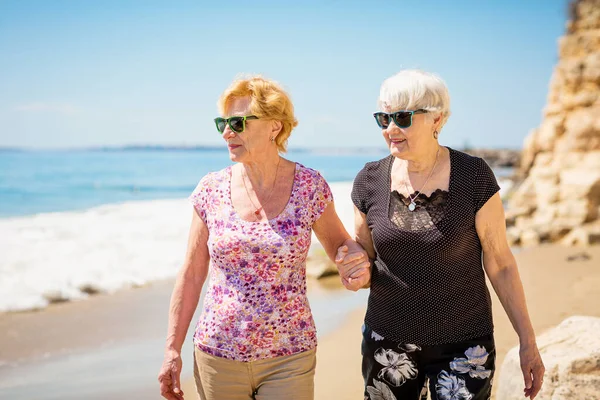 stock image Two elderly women are walking along the rocky shore, talking and laughing, having a pleasant time together