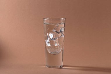 Açık kahverengi zemin üzerinde buz küpleri olan bir bardak saf soğuk, köpüklü su. Metin için boş alan
