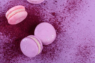Pastel renginde tatlı Fransız kurabiyeleri ve mor arka planda kuru yabanmersini tozu. Pastane ve pastane için güzel bir kompozisyon. Metin için kopyalama alanı olan üst görünüm