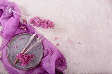 Açık gri arkaplanlı mor kumaşlı leylak çiçekleriyle dolu bir masa. Güzel bahar çiçeği kompozisyonu. Metin için kopyalama alanı olan üst görünüm