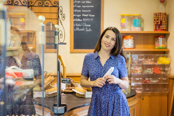 Young pretty woman shopping in a bakery. A customer standing near a showcase with sweets in a store