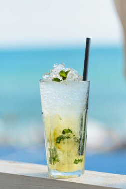 Mavi denize karşı terasta bir bardak Majito kokteyli. Sıcak güneşli bir günde, deniz kenarındaki kafede soğuk bir içecek.