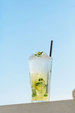 Mavi denize karşı terasta bir bardak Majito kokteyli. Sıcak güneşli bir günde, deniz kenarındaki kafede soğuk bir içecek.