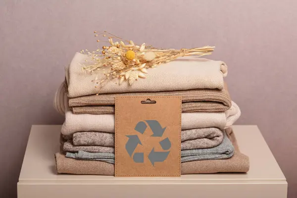 Stack of second hand clothes with used wardrobe for reuse and card with circular economy logo. Reusing, recycling materials and reducing waste in fashion, second hand apparel idea. Zero waste concept