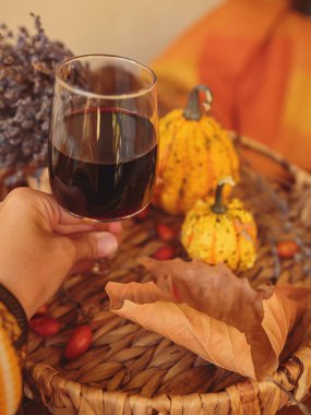 Balkabağı ve kuru yapraklarla süslenmiş ahşap masada bir bardak kırmızı şarap. Şarap kadehi tutan kadınlar. Şükran Günü için sonbahar kompozisyonu. Sonbahar havası