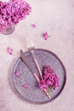 Açık gri arka planda eflatun çiçekli ve mor kumaşlı güzel bir masa. Restoranda romantik akşam yemeği için tatil süsü. Metin için kopyalama alanı olan üst görünüm