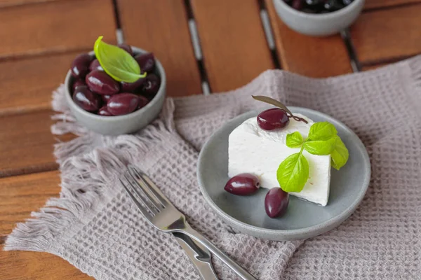 Gri tabakta dilimlenmiş Feta peyniri, siyah zeytin ve fesleğen yapraklarıyla. Terasta lezzetli ve sağlıklı bir kahvaltı.