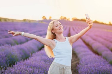 Lavanta tarlası. Sarı saçlı güzel bir kadın cep telefonlu lavanta çiçeklerinin arasında yürüyor, selfie çekiyor, sosyal ağlarda iletişim kuruyor, dinleniyor, dinleniyor, doğanın tadını çıkarıyor.