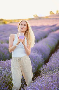 Lavanta tarlası. Sarı saçlı güzel bir kadın yaz aylarında serinletici bir kokteyl bardağıyla lavanta çiçeklerinin arasında yürüyor. Rahatlıyor, dinleniyor, doğanın tadını çıkarıyor. Ruh sağlığı konsepti