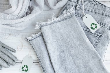 Beyaz ahşap arka planda geri dönüşüm sembolü olan kadın kıyafeti ve kağıt etiket üzerinde üst görünüm. Dairesel moda, çevre dostu sürdürülebilir alışveriş, ikinci el mağazalar konsepti