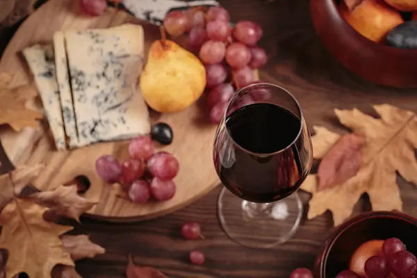赤ワインのグラスは 濃い木の背景に青いチーズを添えました 秋のピクニックとワインとチーズのプラッター 果物と乾燥した葉の素朴なスタイル トップビュー — ストック写真