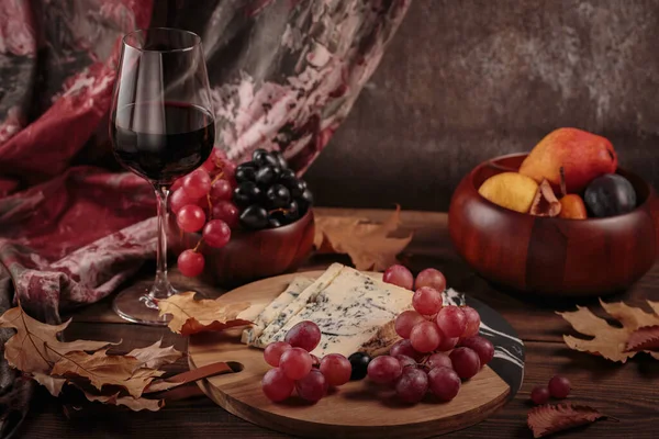 秋天的舒适生活与一杯红酒 奶酪盘 季节性的水果和干燥的叶子 乡村风格在黑暗的木制背景 毛衣天气概念 — 图库照片