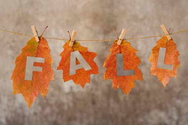 Renkli sonbahar yapraklarından ev yapımı çelenk ve yazıt dökümü. Yapraklar ipe tutunuyor. Duvarda mandallar var. Sonbahar tatilini, Şükran Gününü ve Cadılar Bayramı 'nı kutlamak için ev dekorasyonu.