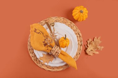 Turuncu arka planda balkabağı süslemeleri olan sonbahar masası. Boş tabak, çatal bıçak takımı, sarı keten peçete ve kuru yapraklar. Sonbahar tatili, Cadılar Bayramı, Şükran Günü konsepti. Üst manzara, düz uzanma