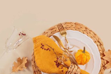 Arka planda balkabağı süslemeleri olan sonbahar masası ayarı. Boş tabak, bardak, çatal bıçak takımı, sarı peçete ve kuru yapraklar. Sonbahar tatili, Cadılar Bayramı, Şükran Günü konsepti. Üst manzara, düz uzanma