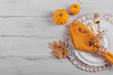 Beyaz arka planda balkabağı süslemeleri olan sonbahar masası. Tabak, çatal bıçak takımı, sarı peçete ve kuru sonbahar yaprakları. Sonbahar tatili, Cadılar Bayramı, Şükran Günü konsepti. Kopyalama alanı olan üst görünüm