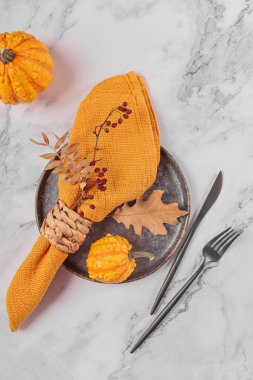 Arka planda balkabağı süslemeleri olan sonbahar masası ayarı. Siyah tabak, çatal bıçak takımı, sarı keten peçete ve kuru yapraklar. Sonbahar tatili, Cadılar Bayramı, Şükran Günü konsepti. Üst manzara, düz uzanma