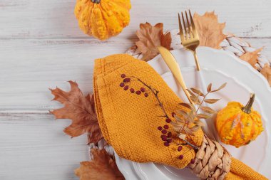 Beyaz ahşap arka planda balkabağı süslemeleri olan sonbahar masası. Boş tabak, çatal bıçak takımı, sarı keten peçete ve kuru yapraklar. Sonbahar tatili, Cadılar Bayramı, Şükran Günü konsepti. Üst görünüm