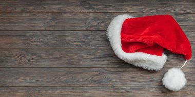 Koyu ahşap arka planda Noel Baba şapkası. Üst görünüm, kopyalama alanı olan uzun pankart