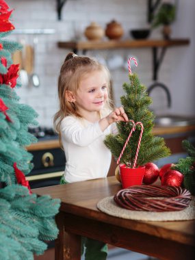 Küçük kız mutfakta Noel ağacı ve yılbaşı dekoruyla oynuyor. Noel, yeni yıl ve kış tatili konsepti