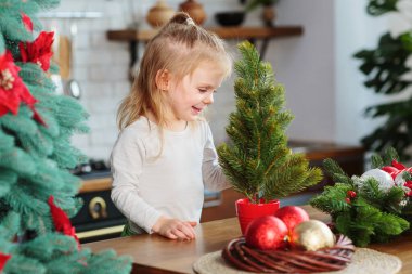 Küçük kız mutfakta Noel ağacı ve yılbaşı dekoruyla oynuyor. Noel, yeni yıl ve kış tatili konsepti