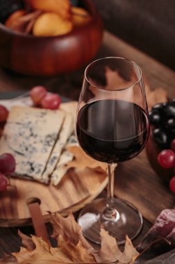 Koyu ahşap arka planda mavi peynirle servis edilen bir bardak kırmızı şarap. Sonbahar pikniği şarap ve peynir tabağı, meyve ve kuru yapraklar kırsal tarzda