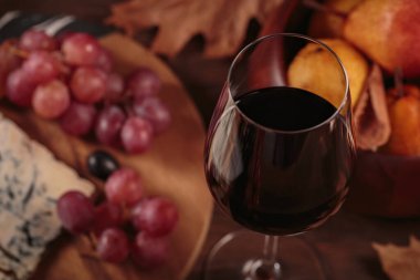 Koyu ahşap arka planda mavi peynirle servis edilen bir bardak kırmızı şarap. Sonbahar pikniği şarap ve peynir tabağı, meyve ve kuru yapraklar kırsal tarzda