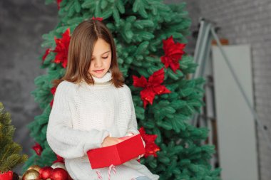 Mutlu, ilgilenen küçük bir kız Noel hediyesini açıyor. Yeni yıl süslenmiş bir mutfakta oturan ve elinde Noel hediyesi tutan bir çocuk.