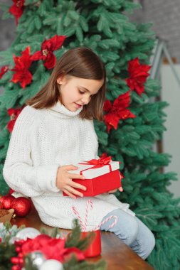 Noel hediyeli mutlu küçük kız. Yeni yıl tatili süslenmiş bir mutfakta oturan ve elinde Noel hediyesi tutan bir çocuk.