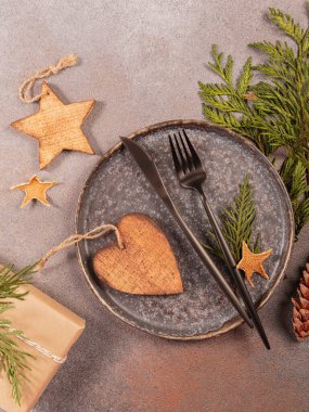 Gri arka planda kış tatili masası. Kara tabak, çatal bıçak takımı, hediye kutusu ve Noel süsü. Kış tatili, Noel, yeni yıl kompozisyonu. Düz yatış, üst görünüm