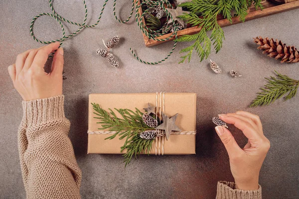 Winter holiday mood, Merry Christmas, Happy New Year background. Preparation for holidays. Wooden box with Christmas decor and Womans hands decorating handmade gift box. Flat lay, top view