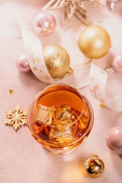 Glass of whiskey or bourbon with festive Christmas decoration on light beige background. New Year, Christmas and winter holidays whiskey mood concept