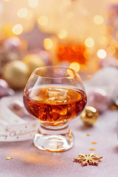Glass of whiskey or bourbon with festive Christmas decoration on light background with bokeh. New Year, Christmas and winter holidays whiskey mood concept