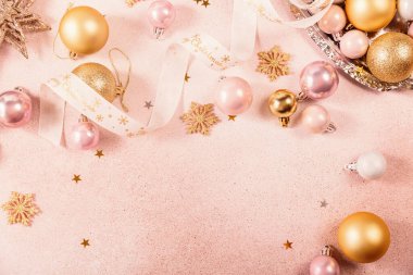 Altın, pembe takılar, kurdeleler ve yıldızlarla dolu Noel ve yeni yıl arkaplanı. Mutlu Noeller yazılı beyaz kurdele. Düz konum, kopyalama alanı olan üst görünüm