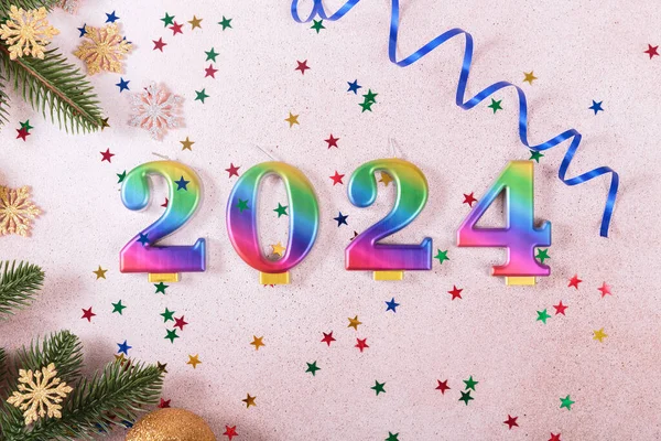 Holiday sparkling background Happy New Year 2024. Rainbow colored candles with numbers of year 2024 on background of festive decor and stars. New Year greeting card. Top view, flat lay