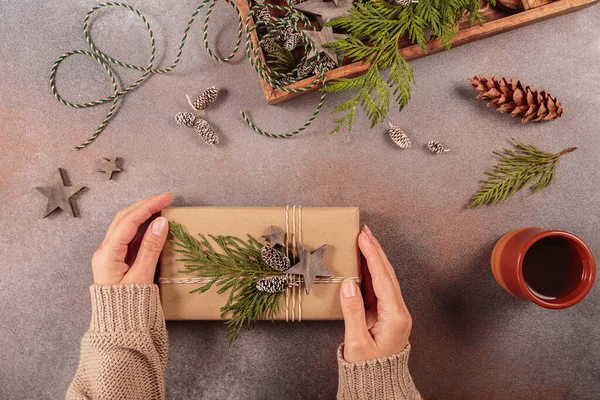 Winter holiday mood, Merry Christmas, Happy New Year background. Preparation for holidays. Wooden box with Christmas decor and Womans hands decorating handmade gift box. Flat lay, top view
