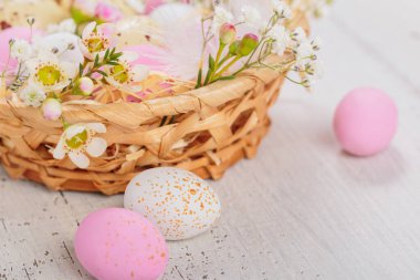 Easter candy chocolate eggs and almond sweets lying in a birds nest decorated with flowers and feathers on white wooden background. Happy Easter concept.