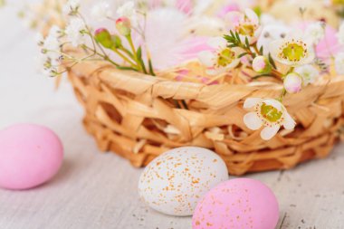 Easter candy chocolate eggs and almond sweets lying in a birds nest decorated with flowers and feathers on white wooden background. Happy Easter concept.