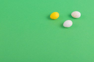 Minimalistic easter background of chocolate candy yellow and white eggs on green background. Top view with free copy space for text