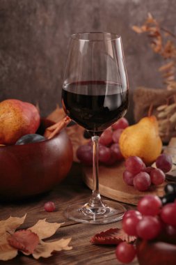 Koyu ahşap arka planda meyvelerle servis edilen bir bardak zengin kırmızı şarap. Sonbahar, şarap, üzüm ve kuru yapraklarla dolu kırsal bir hayat. Süveter hava konsepti