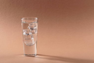 Açık kahverengi zemin üzerinde buz küpleri olan bir bardak saf soğuk, köpüklü su. Metin için boş alan