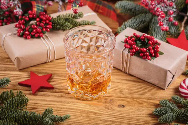 Glass of whiskey or bourbon with festive Christmas decoration on light wooden background. New Year, Christmas and winter holidays whiskey mood concept