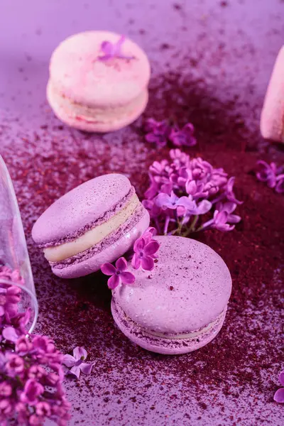 Pastel renginde, üzerinde leylak çiçekleri ve mor arkaplanda kuru yaban mersini tozu bulunan tatlı Fransız kurabiyelerine yakın çekim yapın. Pastane ve pastane için güzel kompozisyon