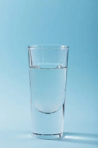 Glass of pure sparkling water on light blue background. Vertical photo with trendy shadows