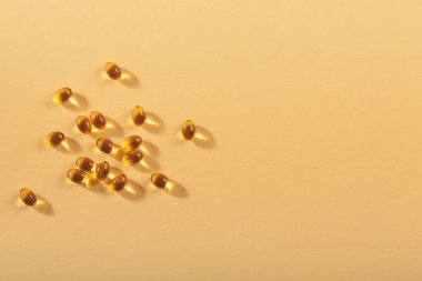 Diyet, beslenme, sağlıklı yeme konsepti. Küçük yağ dolu sarı yumuşak kapsüller bej arka planda gıda takviyeleri.