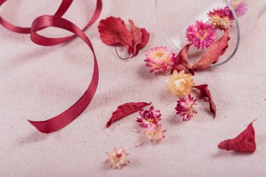 Kurdele ve kırmızı kurumuş çiçeklerle dolu cam kadehten sonbahar kompozisyonu ve bej arka planda yapraklar. Sonbahar arkaplanı