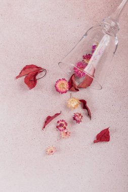 Kırmızı kurumuş çiçeklerle dolu cam kadehten sonbahar kompozisyonu ve bej arka planda yapraklar. Sonbahar arkaplanı